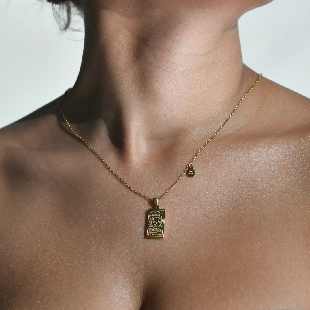 AQUARIUS Zodiac Pendant Gold Necklace. Rectangular shape pendant with an aquarius symbol vase engraved on top of it, the aquarius word written on the bottom. one side of the gold chain has a small round aquarius symbol attached, The pendnat is droped in a gold chain.