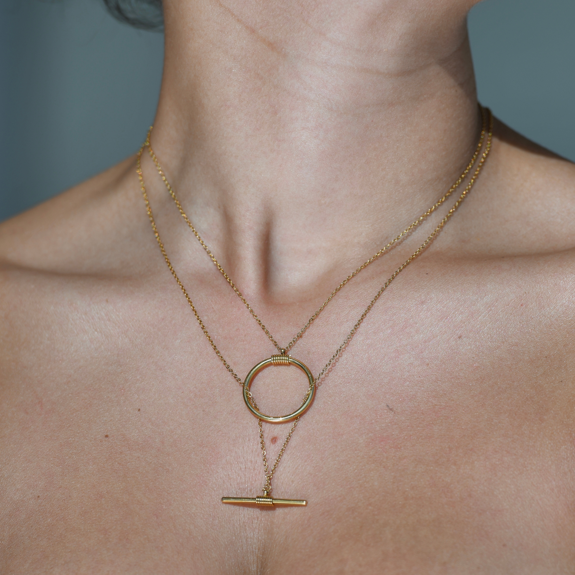 BALANCE Pendants Gold Necklace -gold pendant consisting of two parts. One chain has a metal hanging in the shape of a circle which comes shorter and the other chain has a horizontal metal hanging which comes longe