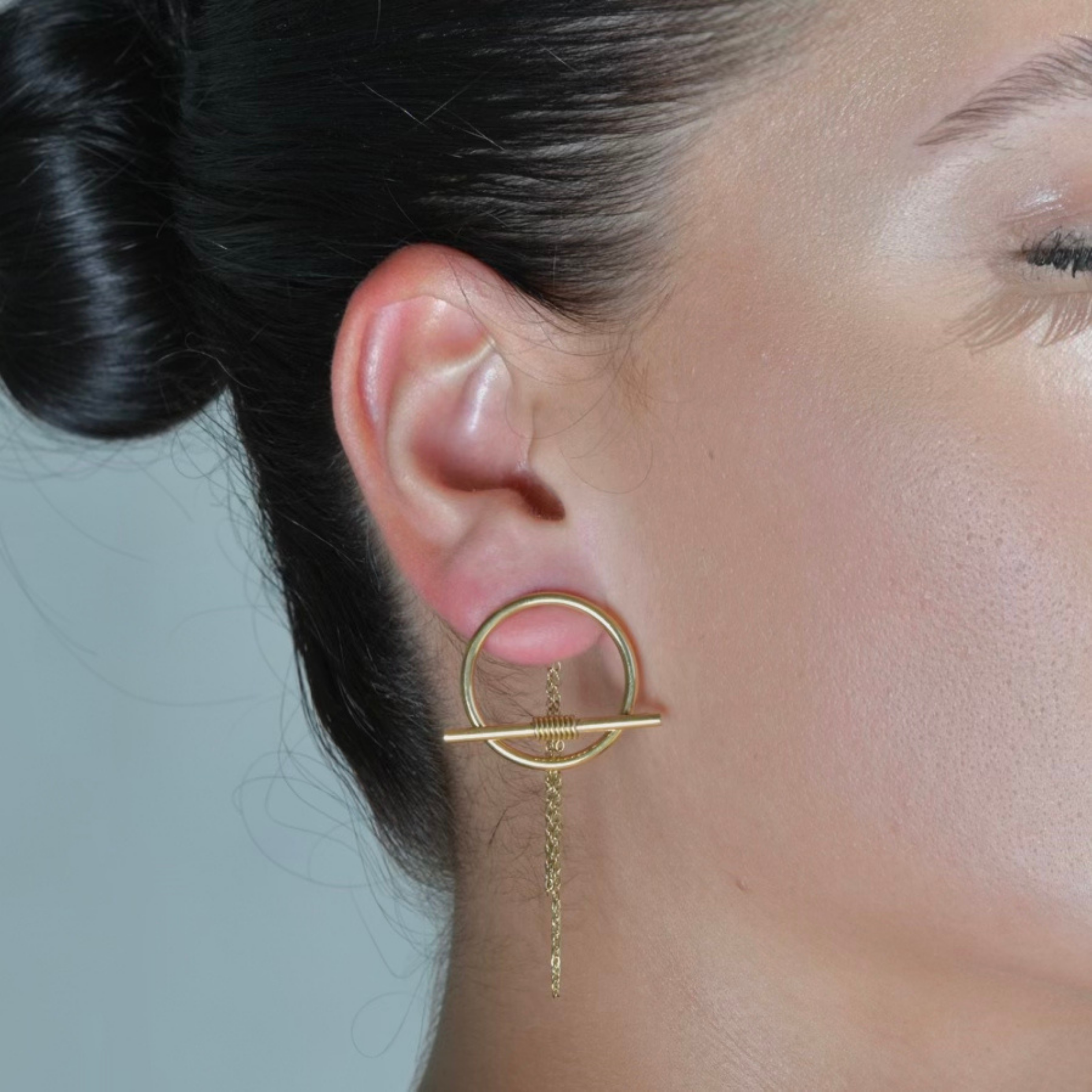 Balance Gold Earrings in the Shape of a gold circle with chain fallen from the top of the circle attached in the post at the back of the earring and a T shape metal attached in the bottom of the cirlce