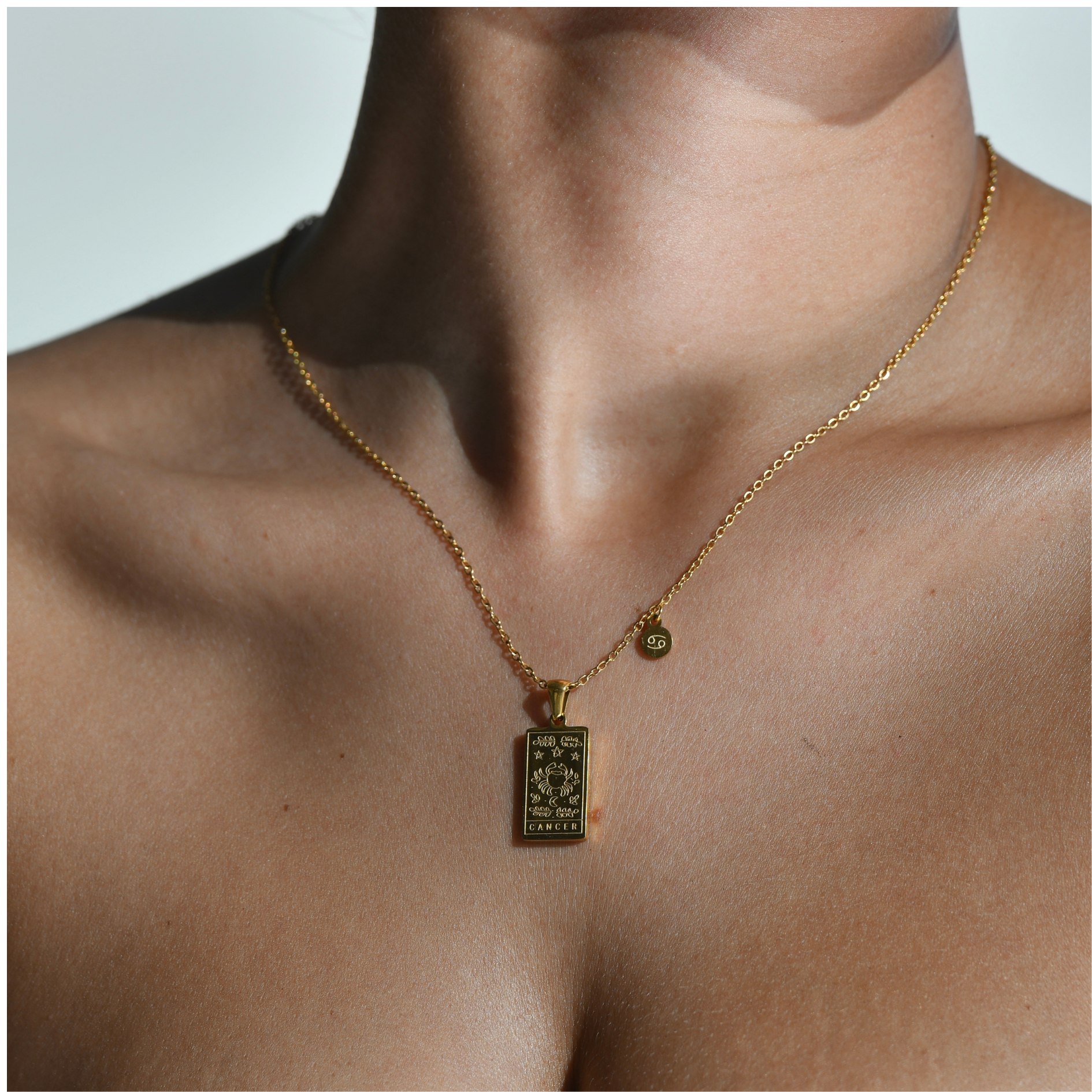 CANCER ZODIAC PENDANT GOLD NECKLACE gold pendant with a pendant hanging in a rectangular shape where the zodiac sign of the crab is engraved and the word crab is engraved at the bottom of the pendant. In the corner of the chain, next to the rectangular pendant, there is a small circle hanging with the symbol of the sign of the crab.