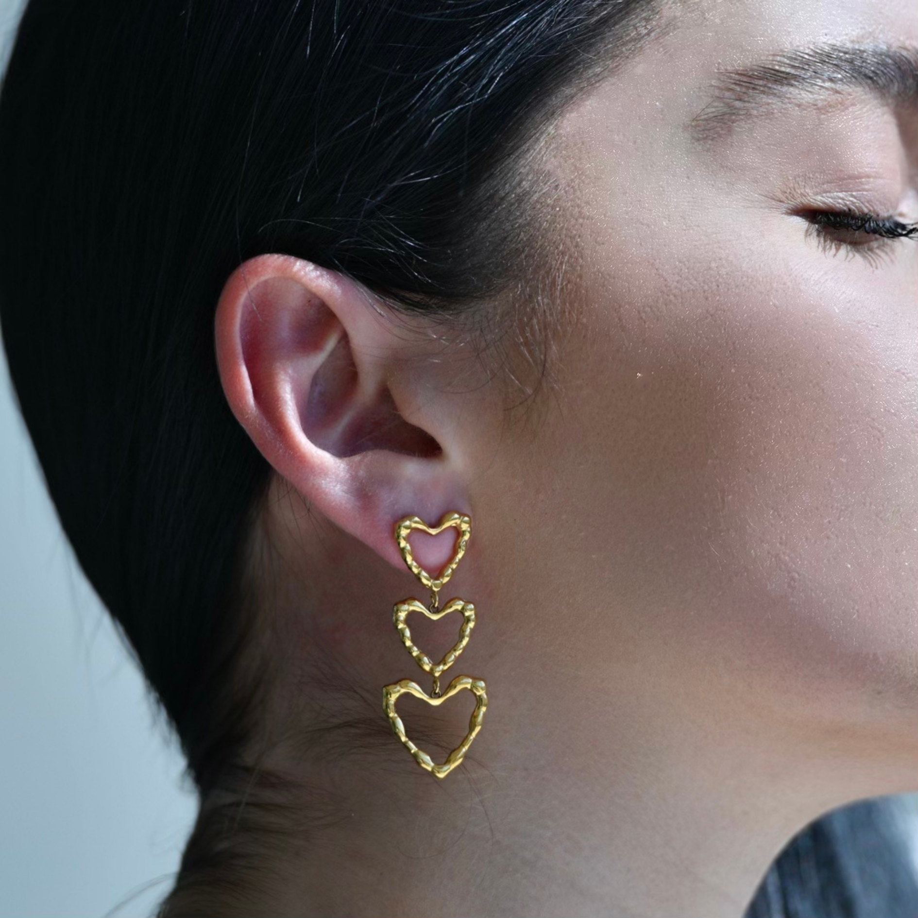 three heart shapes hanging one after the other. The biggest heart hangs at the end of the earrings. The surface is inspired by sand dunes. The hearts are empty on their surface, only the outer frames have metal.