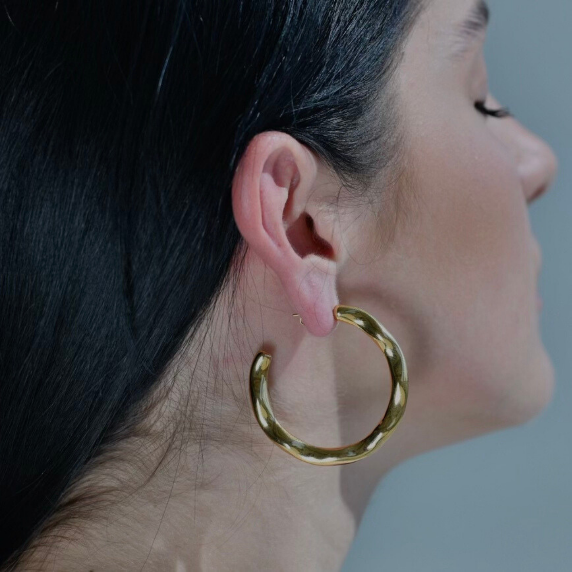 woman wearing Gold hoop earrings with irregular surface. Big size of gold round earrings. Irregular surface.