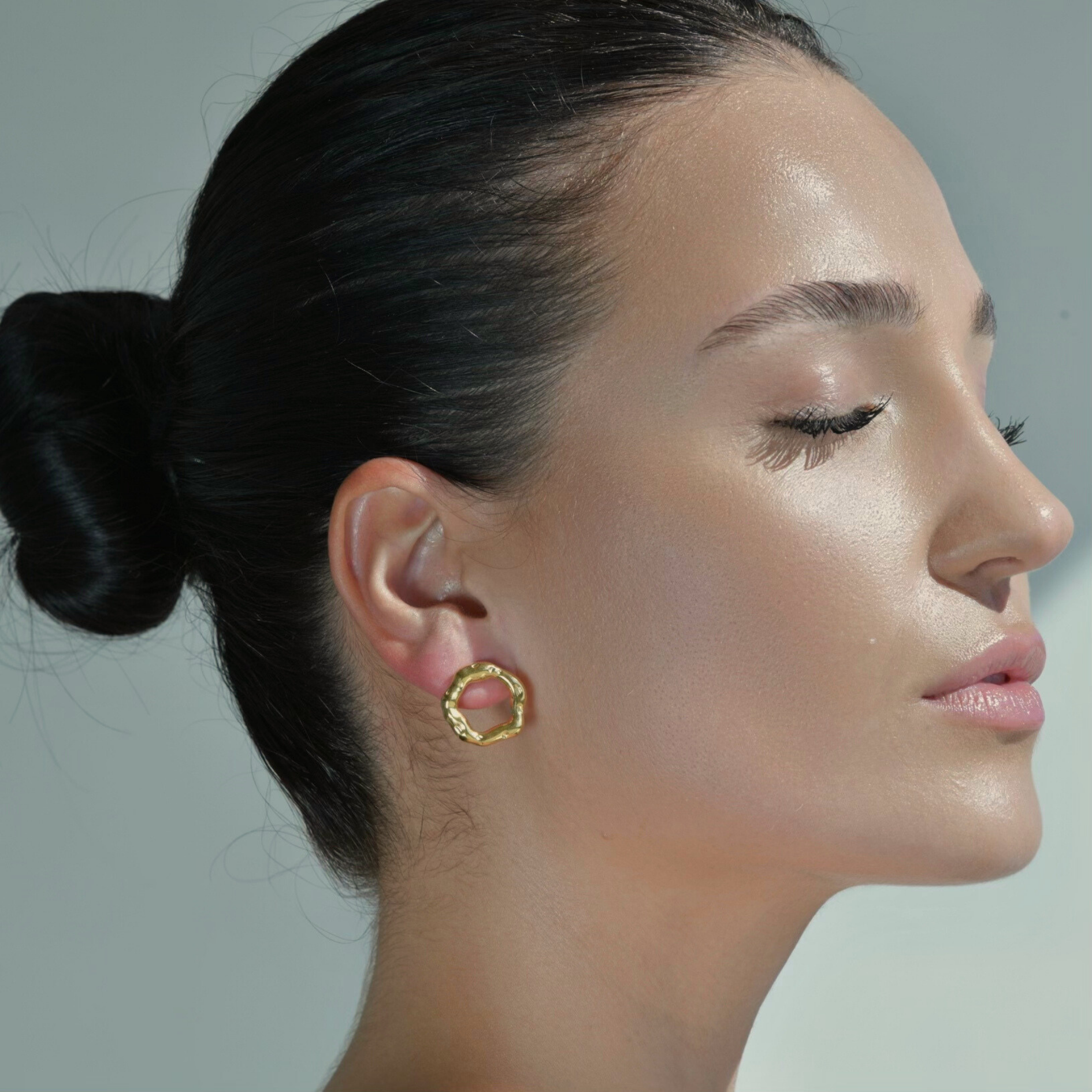Woman Wearing Circle Earrings with irregular shape. Gold plated with texture that imitates movement.