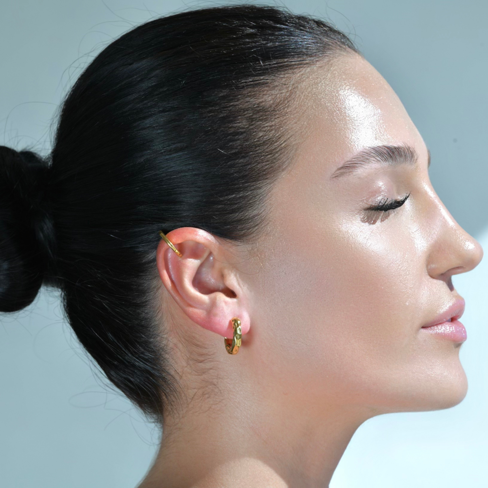 Woman wearing a gold cuff and the Gold Huggies Earrings, Hoop circle earrings with irregilar border texture. The surface texture Resembles waterdrops on the sand