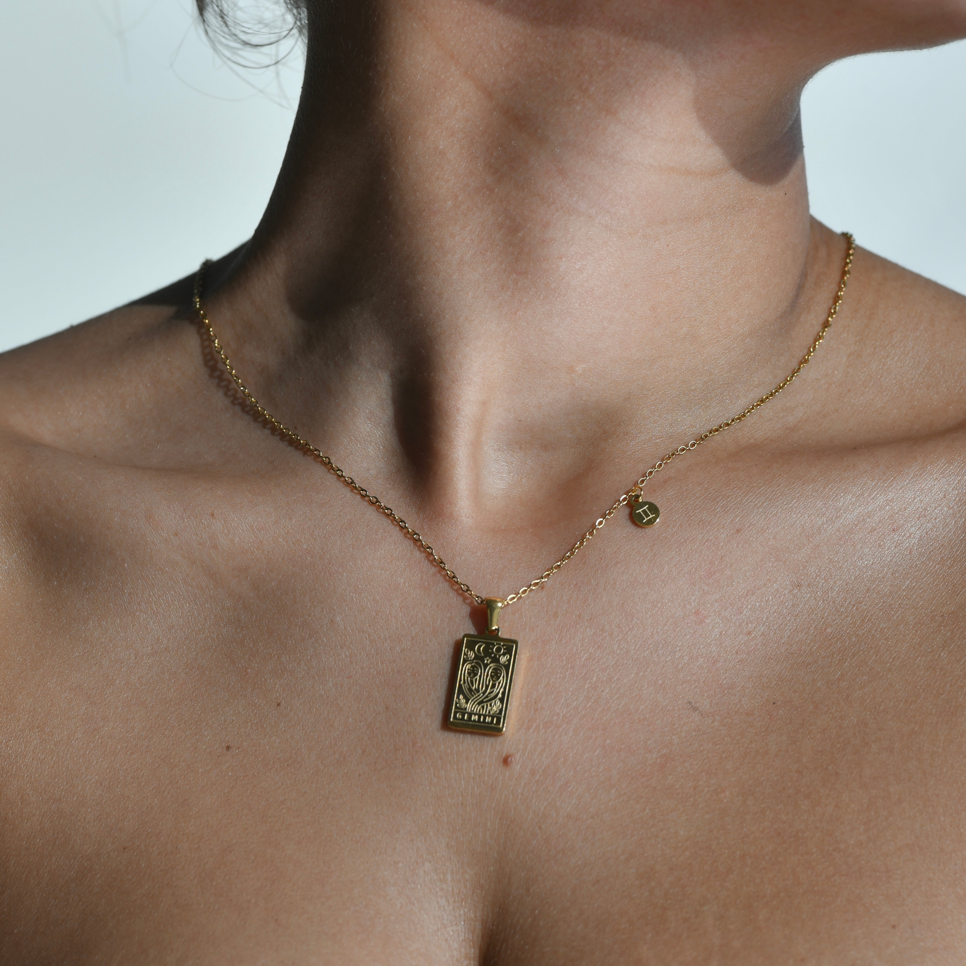 GEMINI Zodiac Pendant Gold Necklace - Gold chain necklace with gemini engraved in a vertical rectangular shape pendant. at the bottom of the pendant is engraved the word "gemini". on the side of the pendant at the chain is attched a square charm with gemini symbol engraved on it.