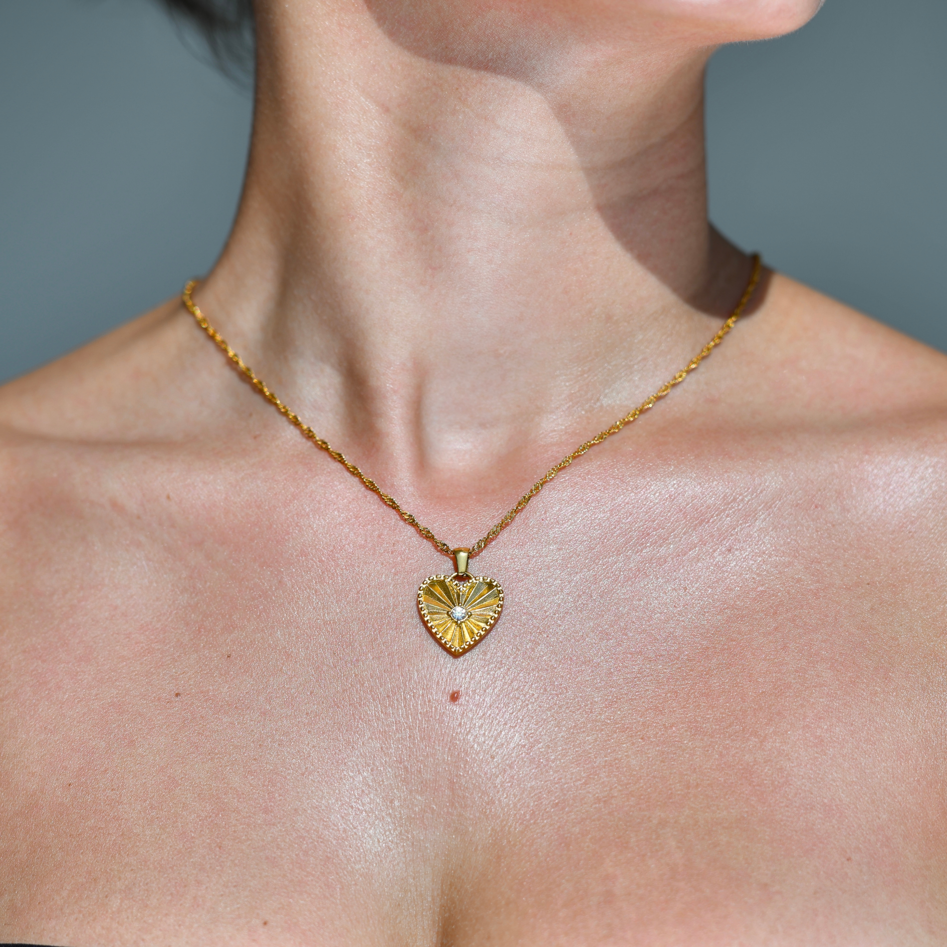 Gold plated waterproof  chain necklace with a heart pendant droping on the chain. A zircon stone in the middle of the heart. The heart has engraved rays pattern starting from the middle opening the borders of the gold heart. Heart Pendant gold necklace.