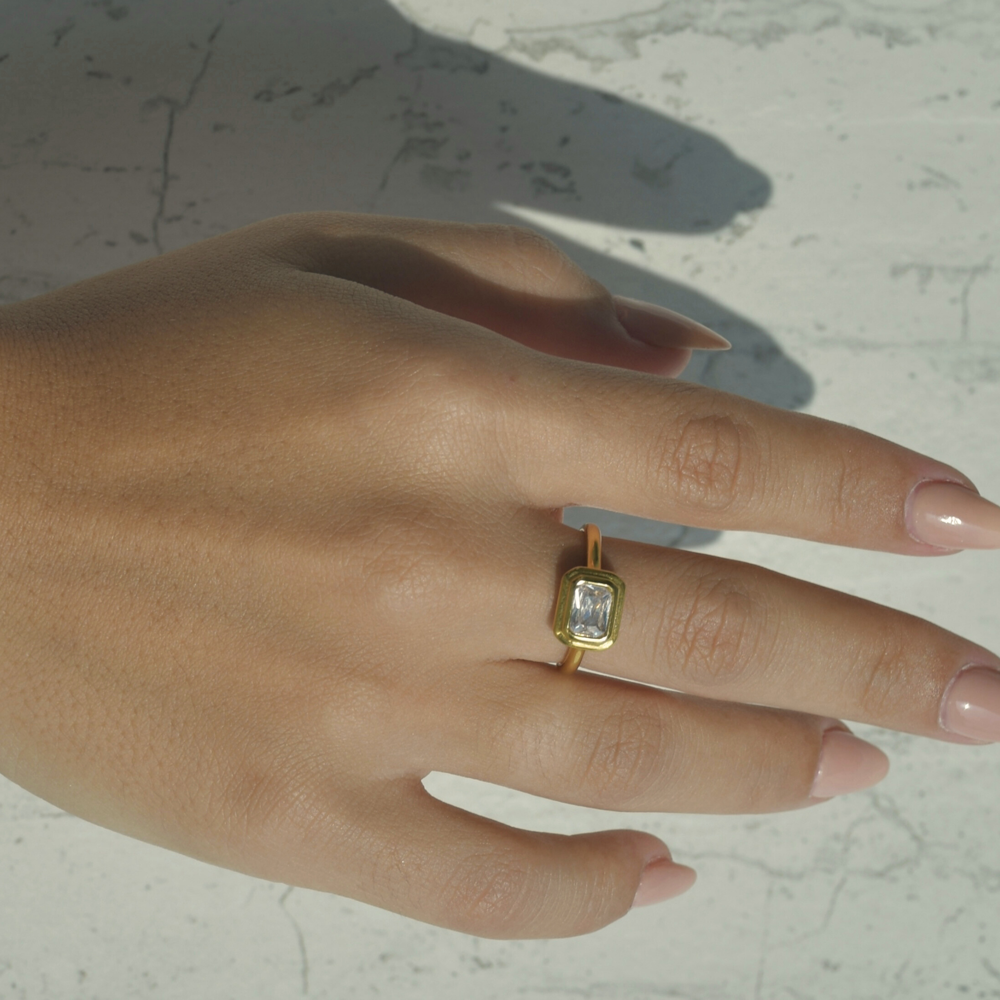 Gold halo ring with a rectangular zircon on the top of the ring.