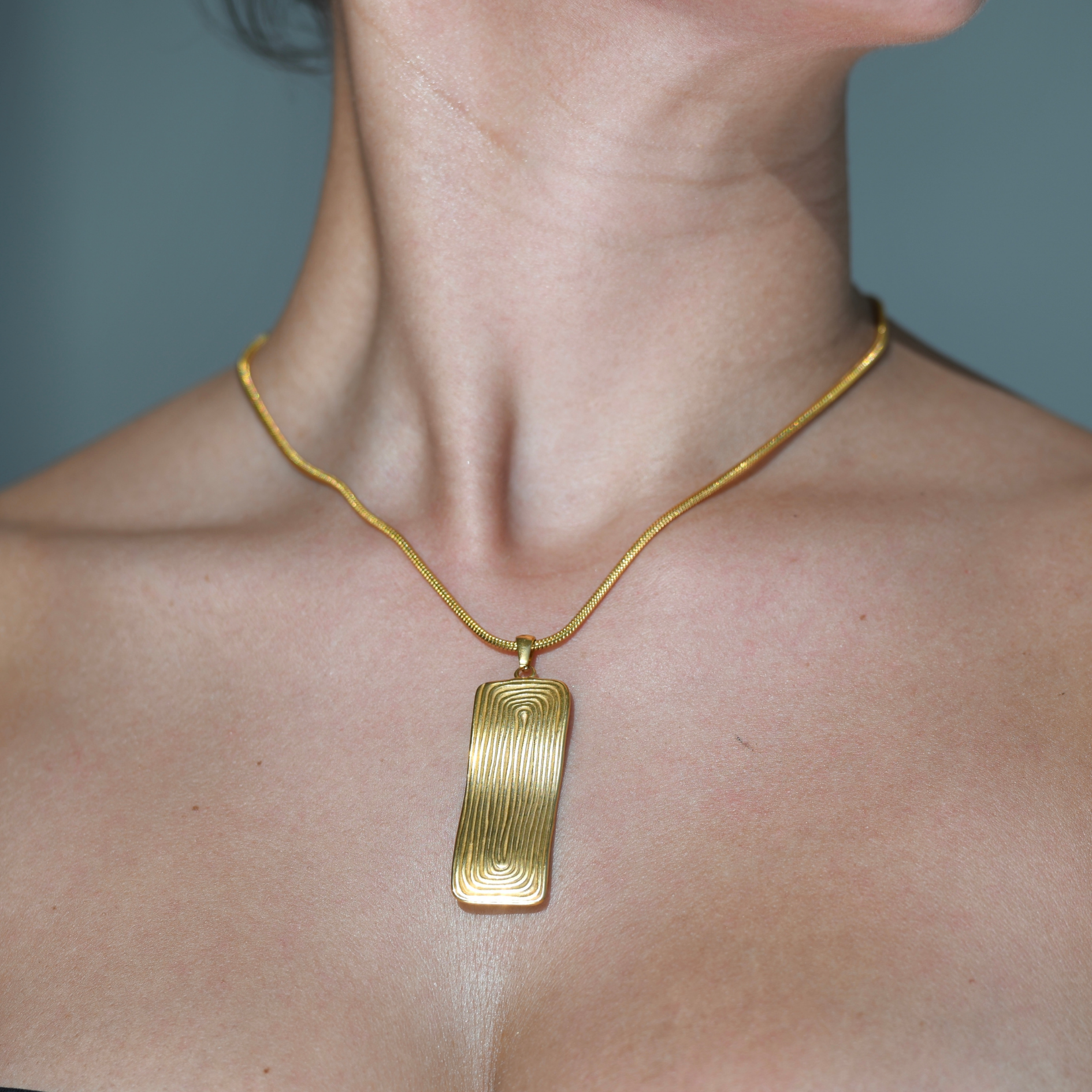 Gold plated chain necklace. An irregular shape bold rectangular pendant drops on the chain. Circular oval shape are engraved on the pendant. Maya pendant gold waterproof necklace.
