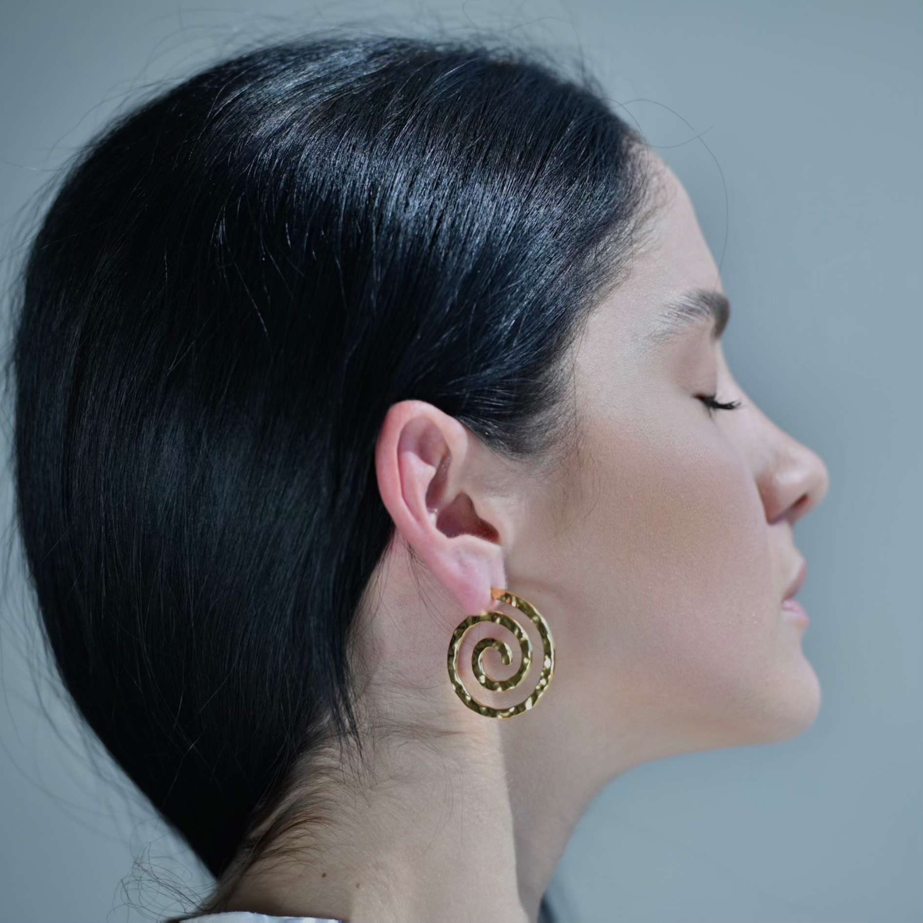 Gold plated hoop earrings with the shape of a spiral. The surface testure is irregular.