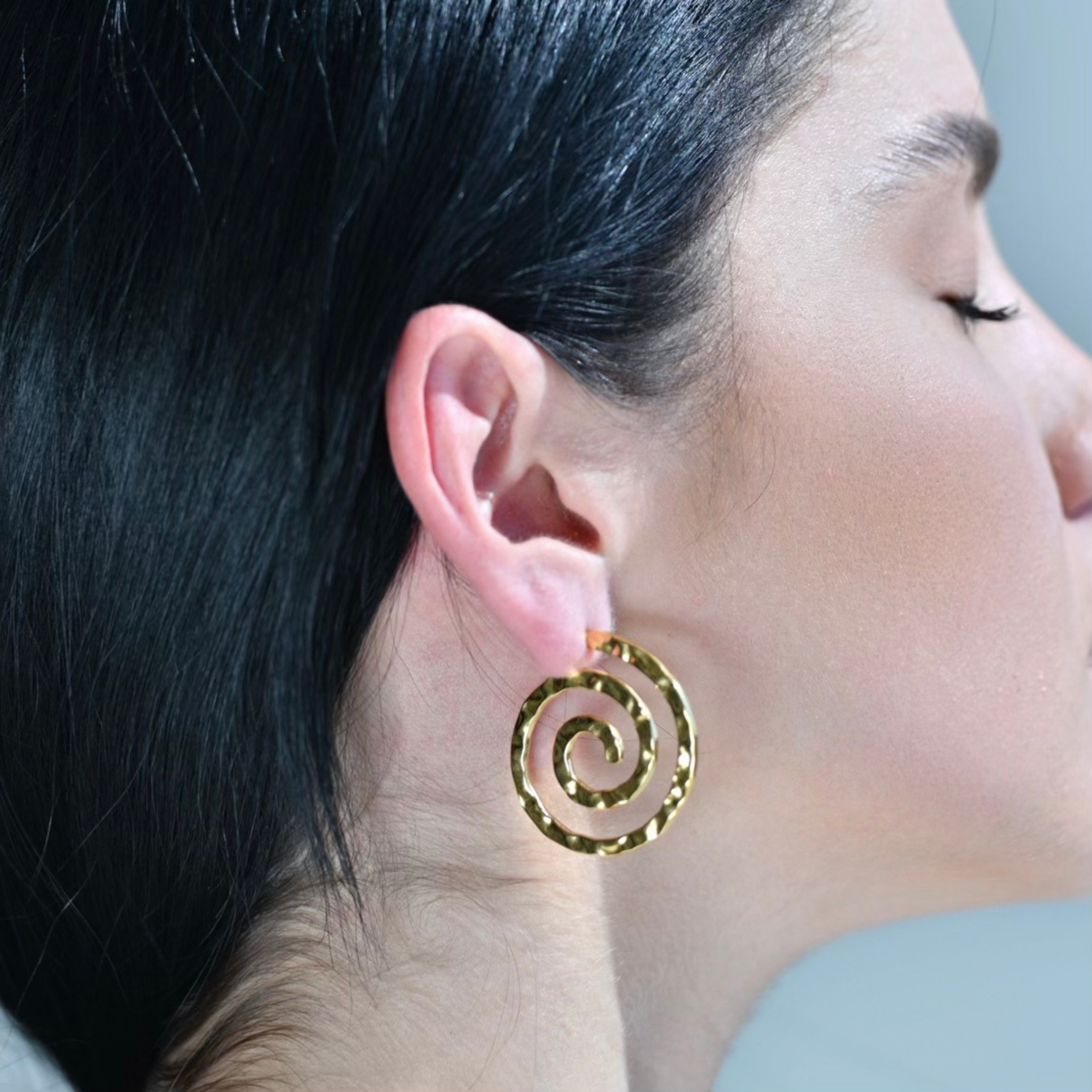 Gold plated hoop earrings with the shape of a spiral. The surface testure is irregular.