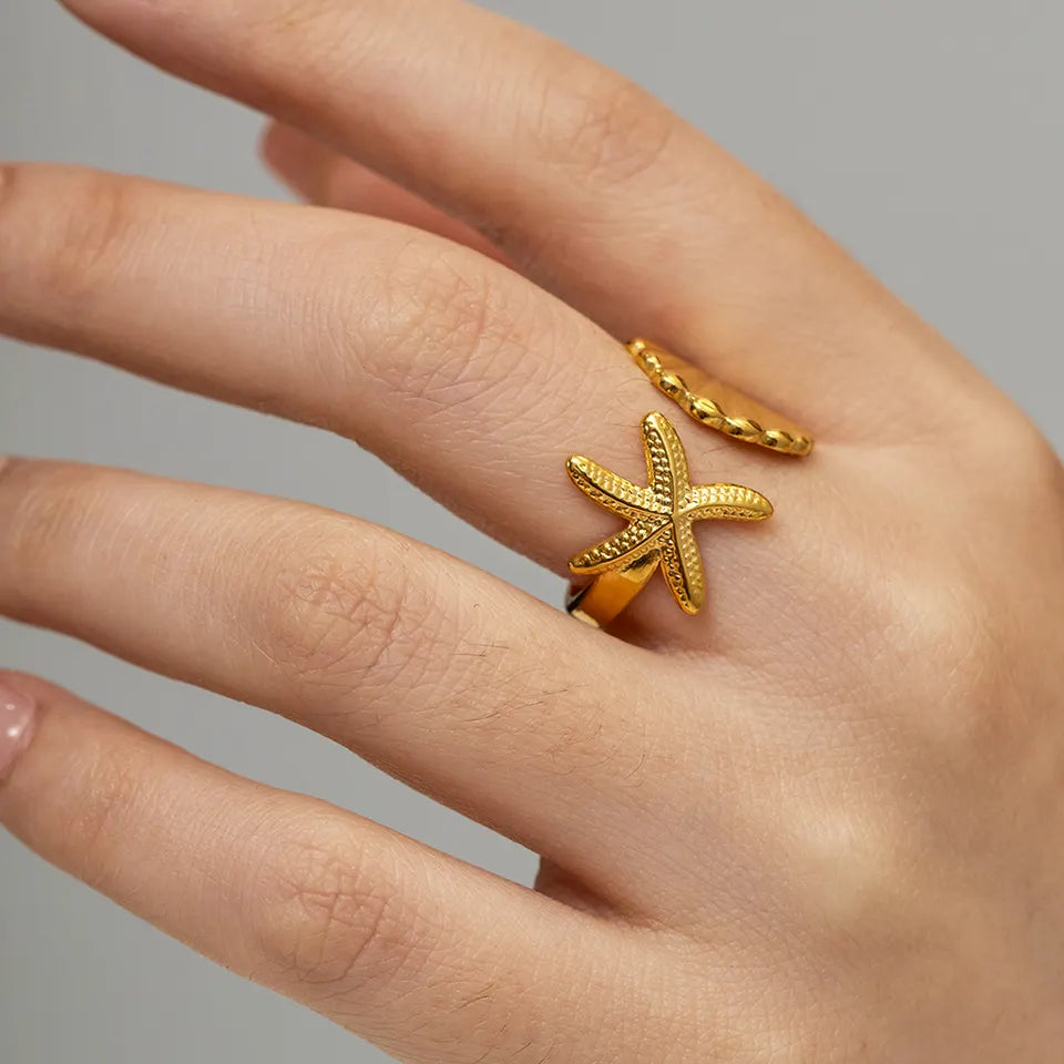 ISLE star and shell gold adjustable ring. A star fish on one side of the rinf and a shell on the other one. The front pf the ring is adjustable open space.