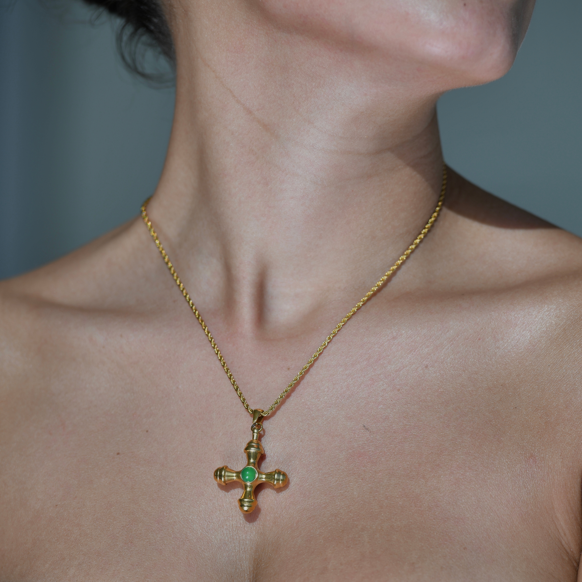 gold plated rope chain necklace. A gold cross hangs on the chain. In the middle of the cross is a green stone.