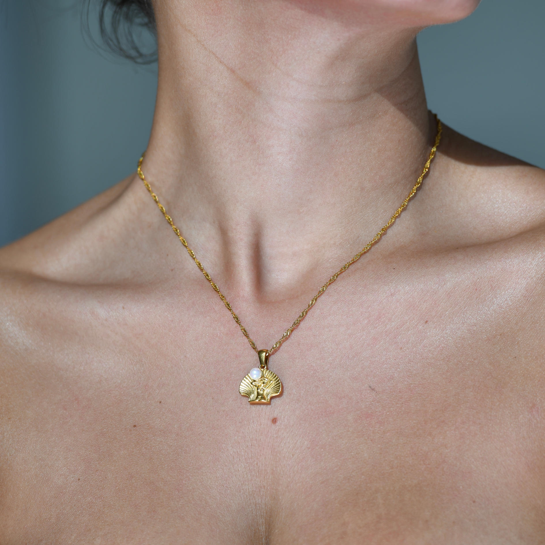 Open Shell Shape pendant with a woman silohuette in the middle holdin a white pearl on her shoulders. Resembling "the birth of venus" Gold plated chain and pendant necklace. Venus shell pendnat gold necklace.