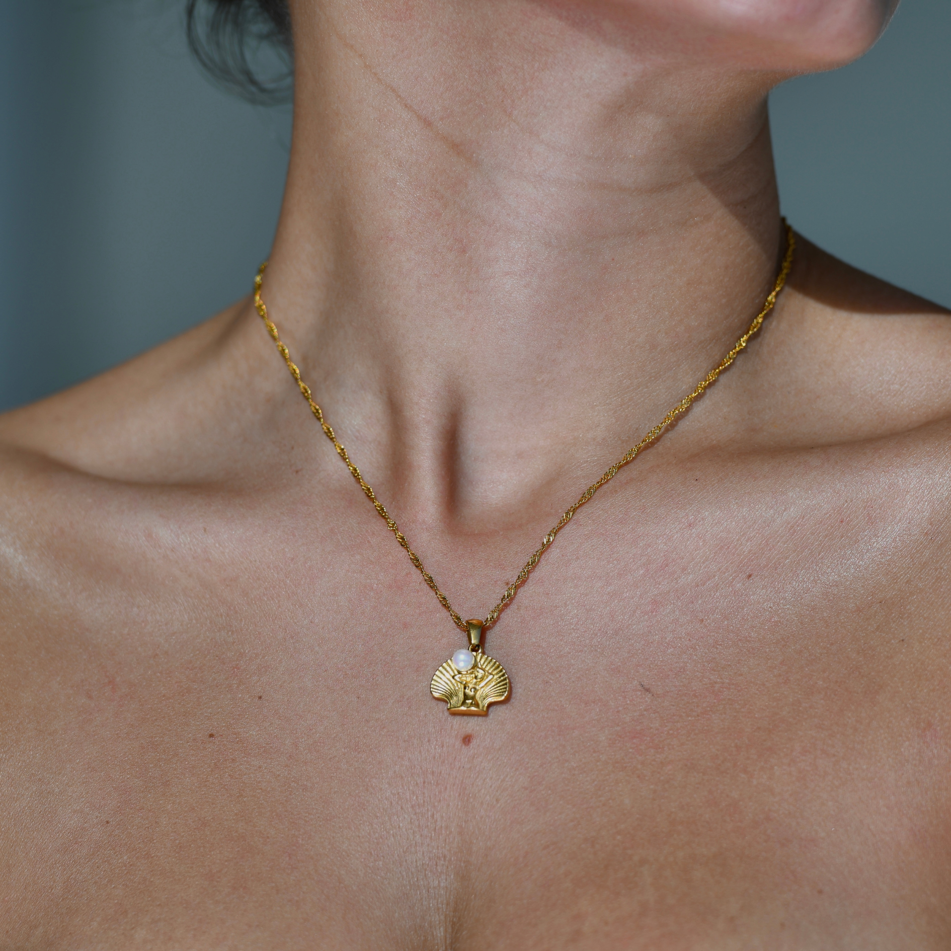 Open Shell Shape pendant with a woman silohuette in the middle holdin a white pearl on her shoulders. Resembling "the birth of venus" Gold plated chain and pendant necklace. Venus shell pendnat gold necklace.