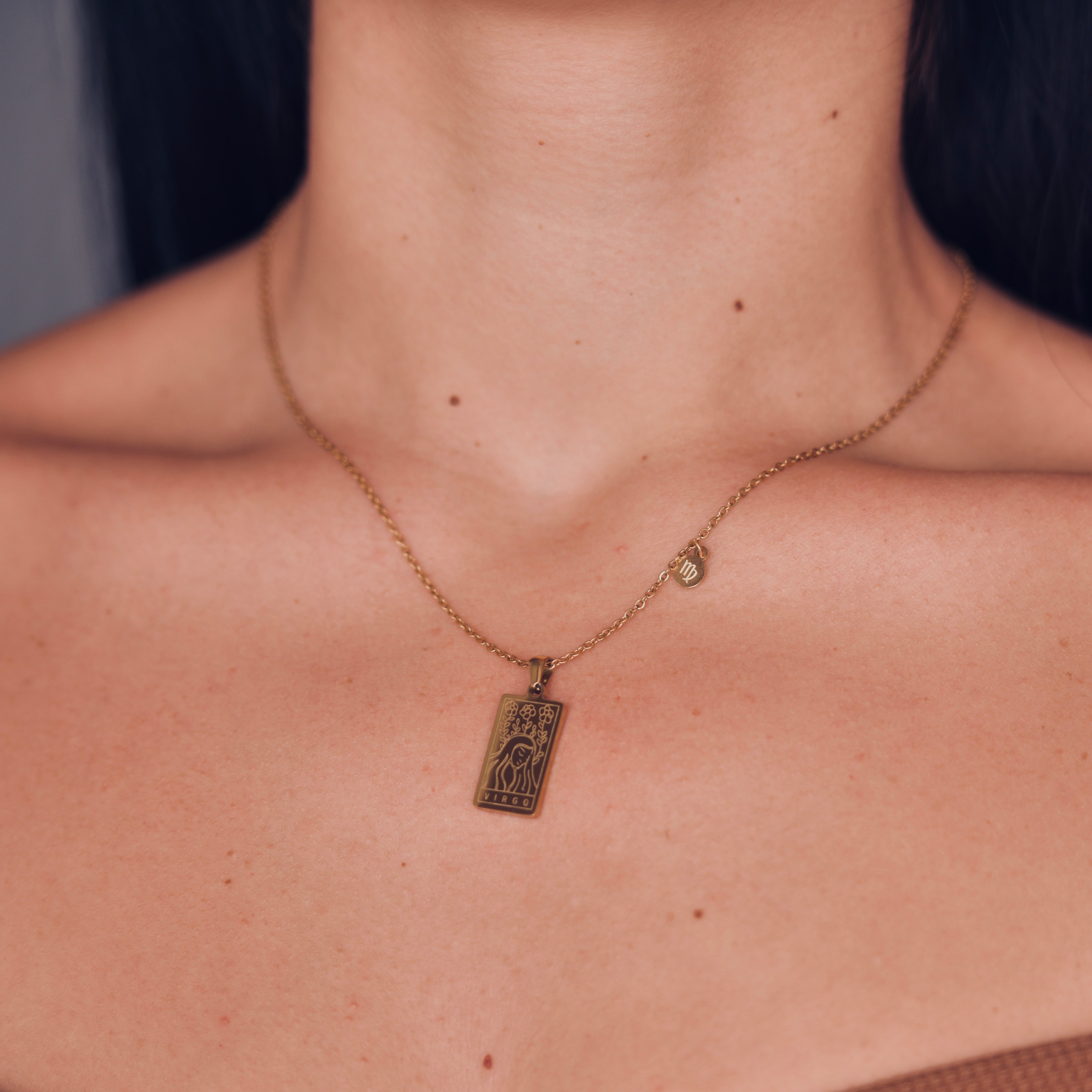 Rectangular gold pendant with a woman engraved representing virgo and the word virgo in the bottom. Gold pendant with a chain necklace. In the side of the gold pendant is a circle small medalion with the symbol of virgo engraved on it. Virgo zodiac pendant gold necklace.