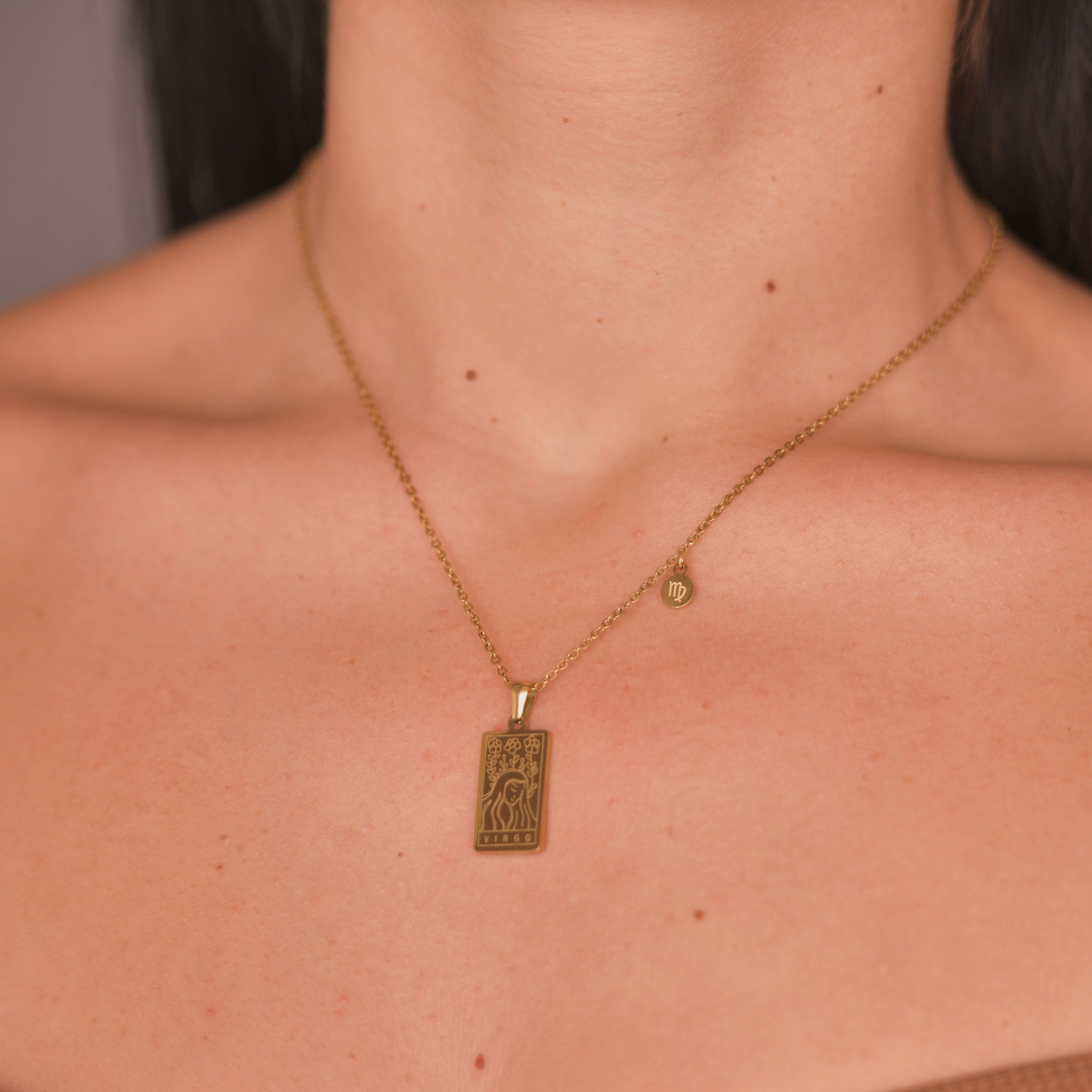 Rectangular gold pendant with a woman engraved representing virgo and the word virgo in the bottom. Gold pendant with a chain necklace. In the side of the gold pendant is a circle small medalion with the symbol of virgo engraved on it. Virgo zodiac pendant gold necklace.